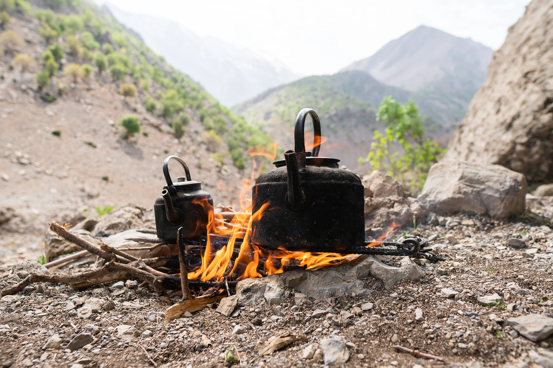 Kampvuurtje met twee pannen op stenen tussen bergen
