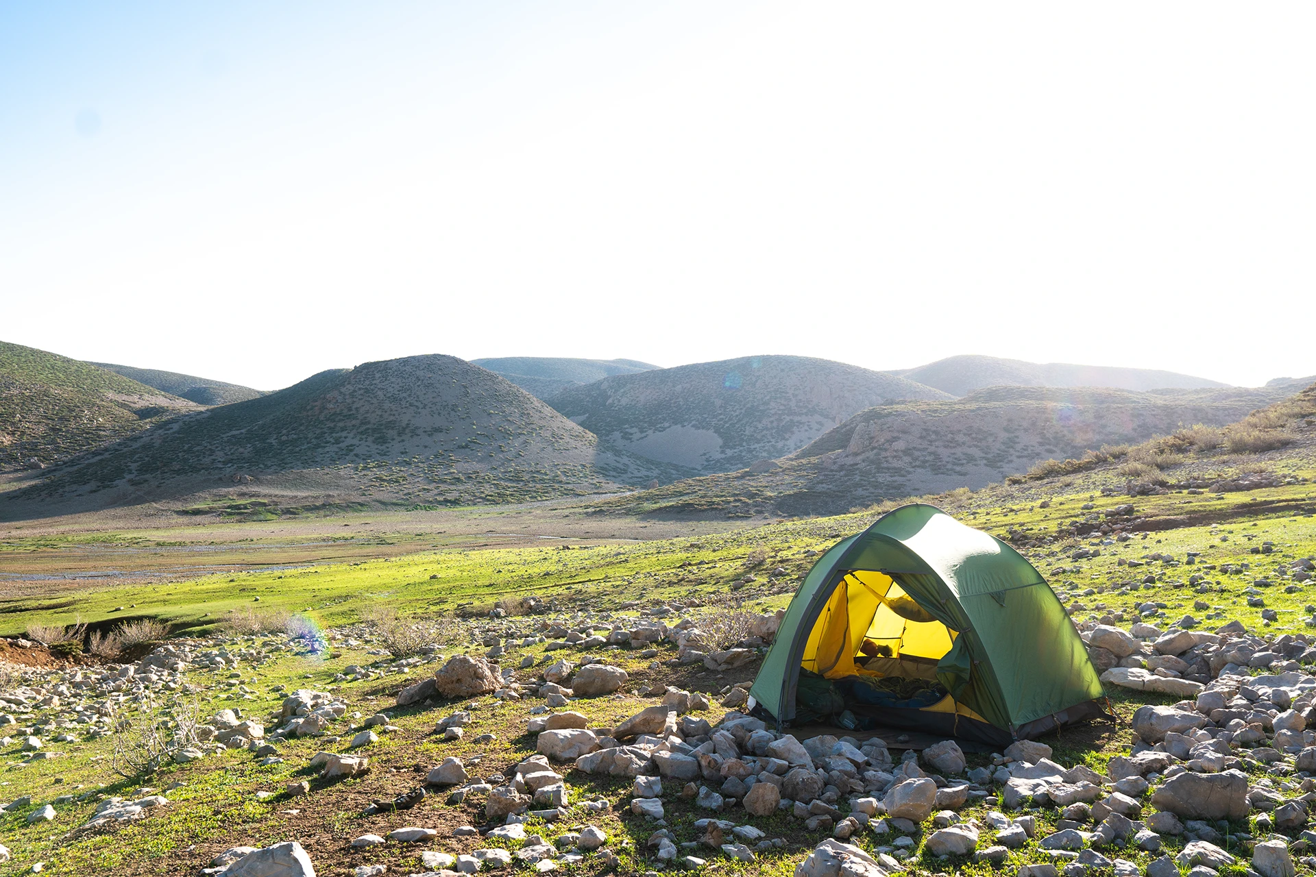 Tent in ochtendlicht op een groene grasvlakte tussen bergen