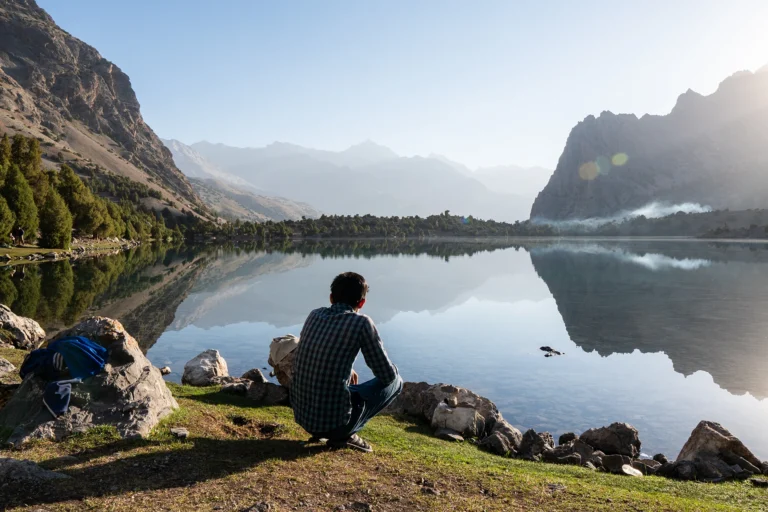 Persoon die zit en uitkijkt over spiegelend bergmeer
