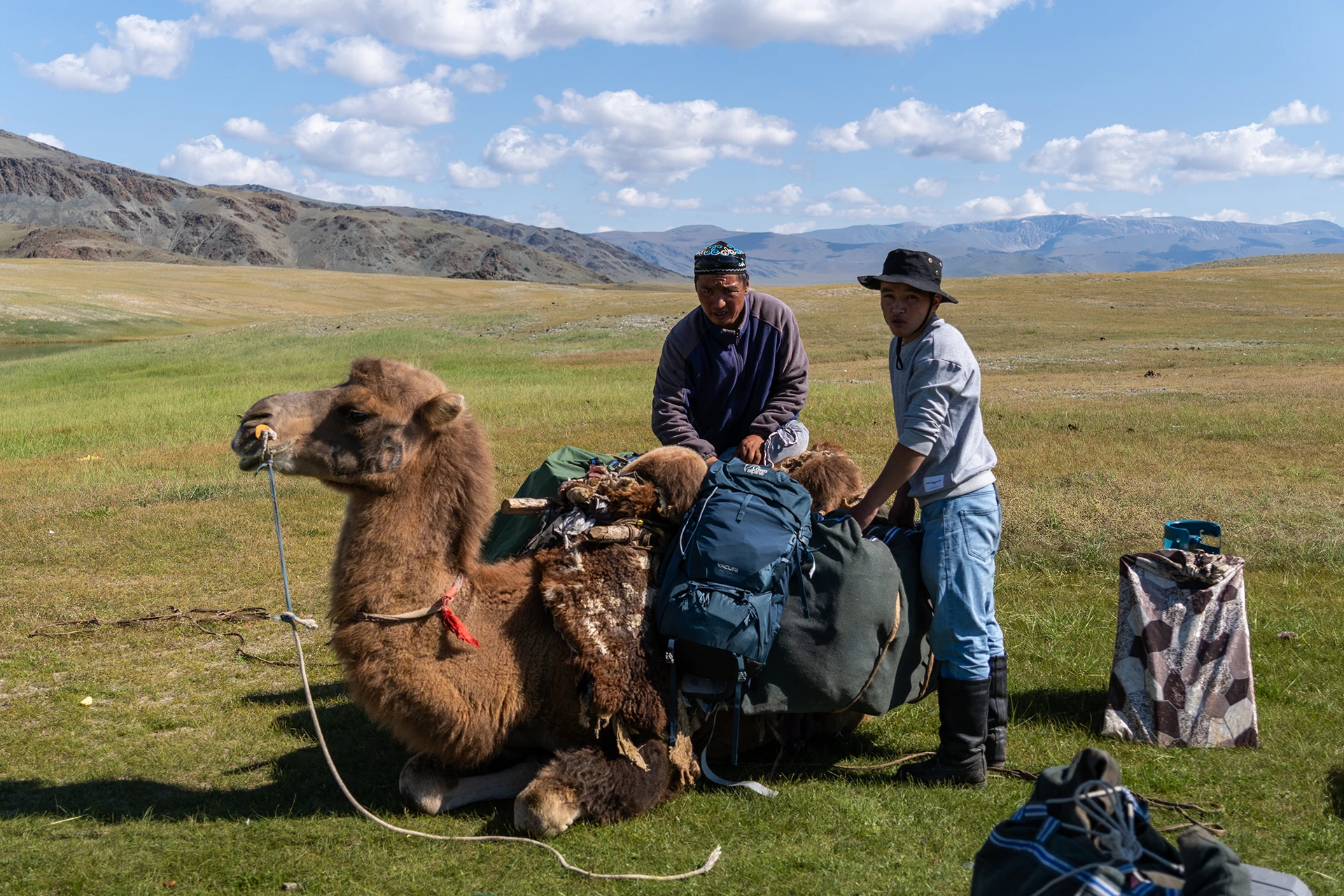Twee mannen die naast een kameel poseren met bepakking