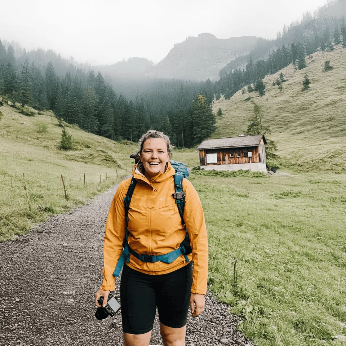 Wandelaar staat op pad in groene vallei met berghut