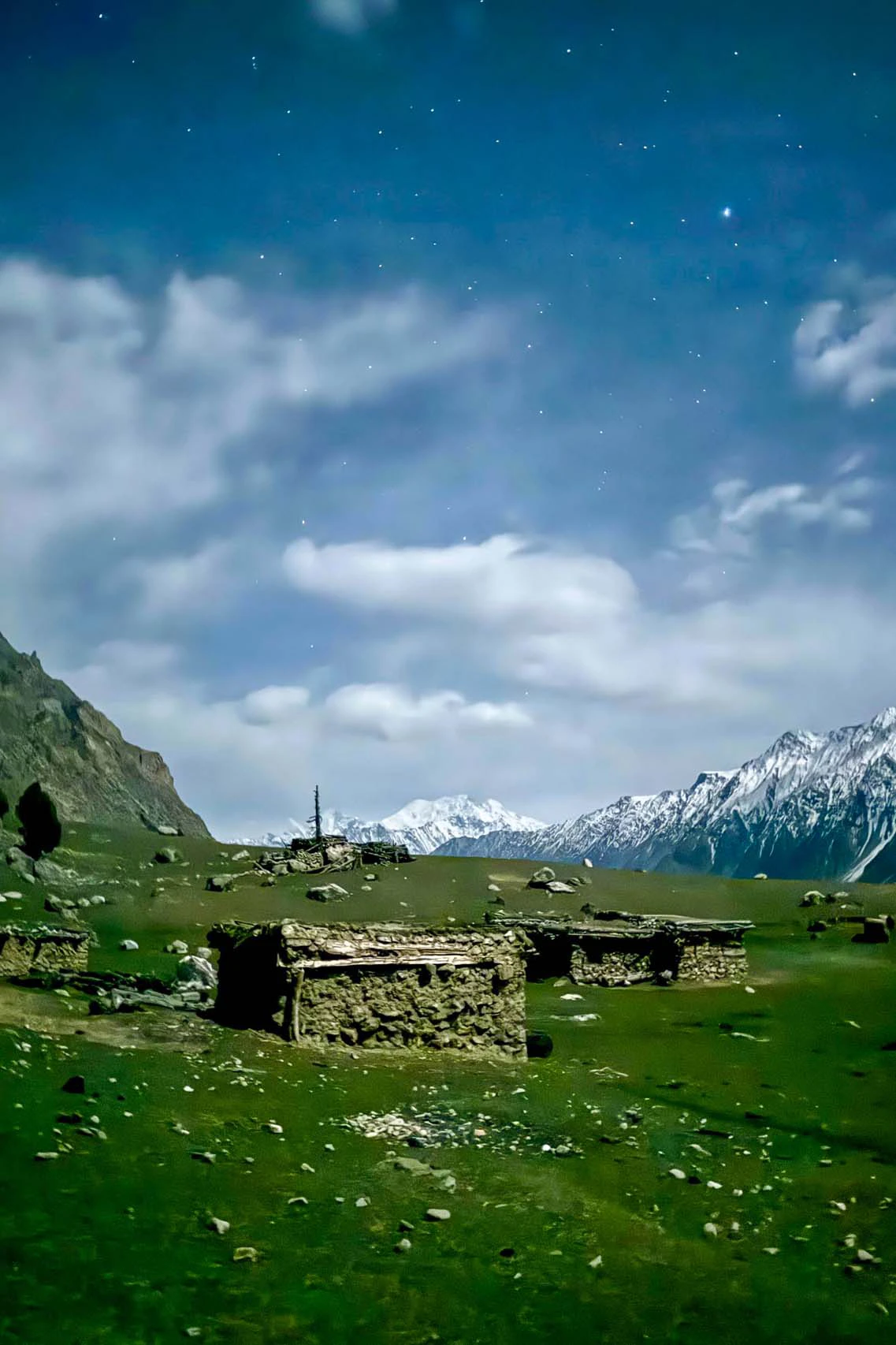 Groene alpenweide met verspreide stenen hutten en wolkenlucht