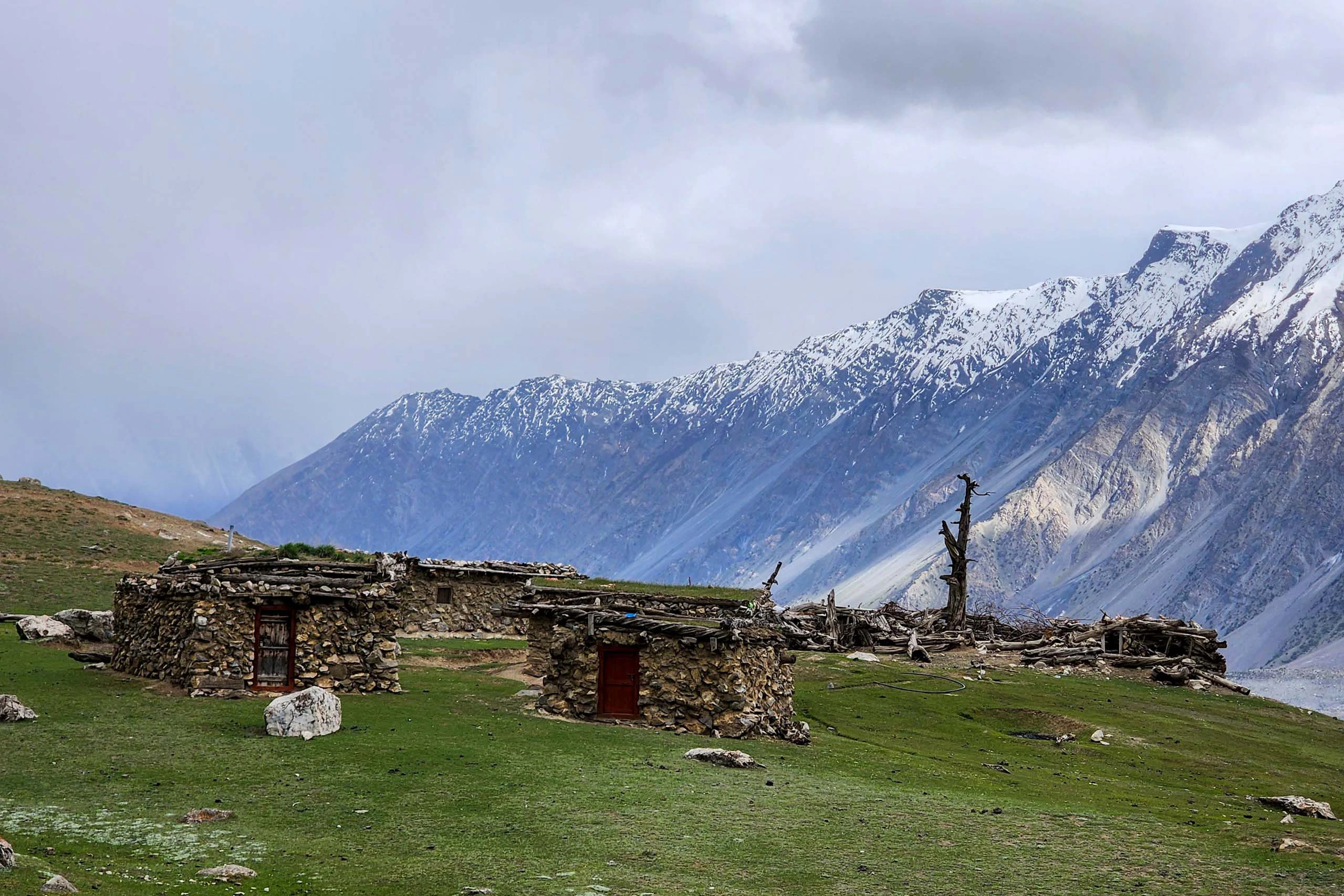 Groene weide met stenen huisjes en besneeuwde bergen in de verte