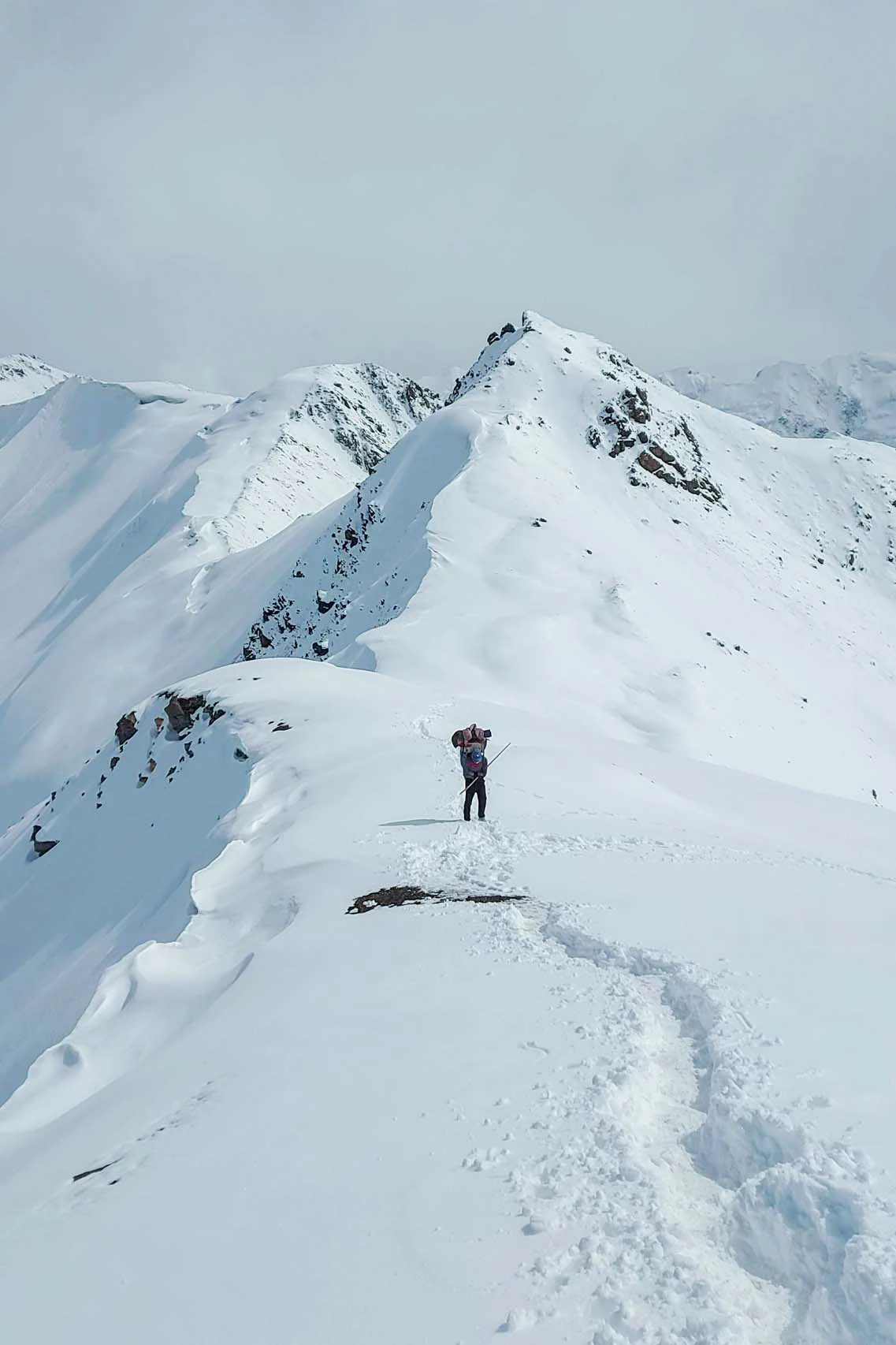 Alleenstaande wandelaar op een smalle besneeuwde berggraat met uitzicht op dalen