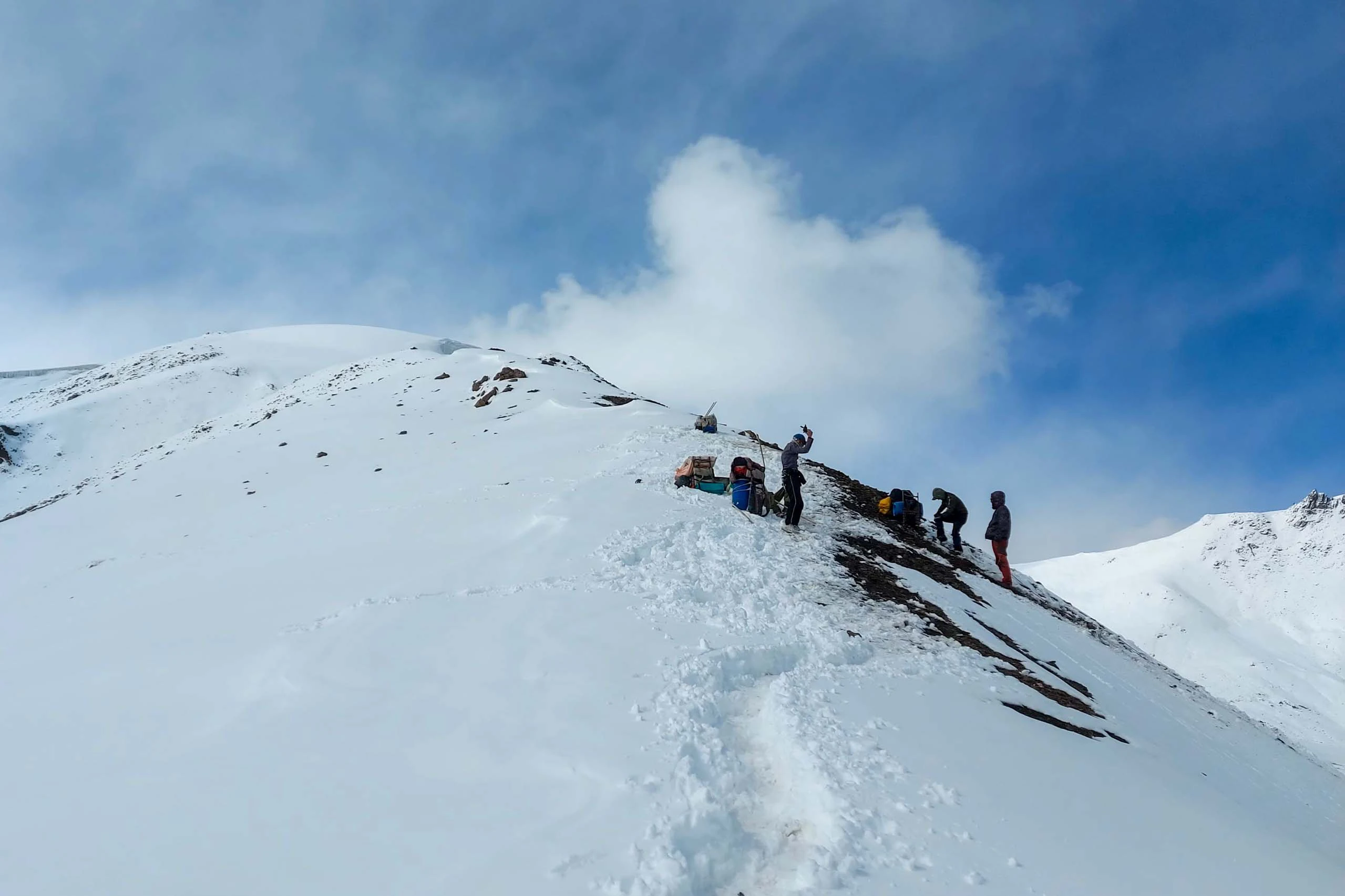 Groep wandelaars loopt in een spoor door diepe sneeuw op een bergkam