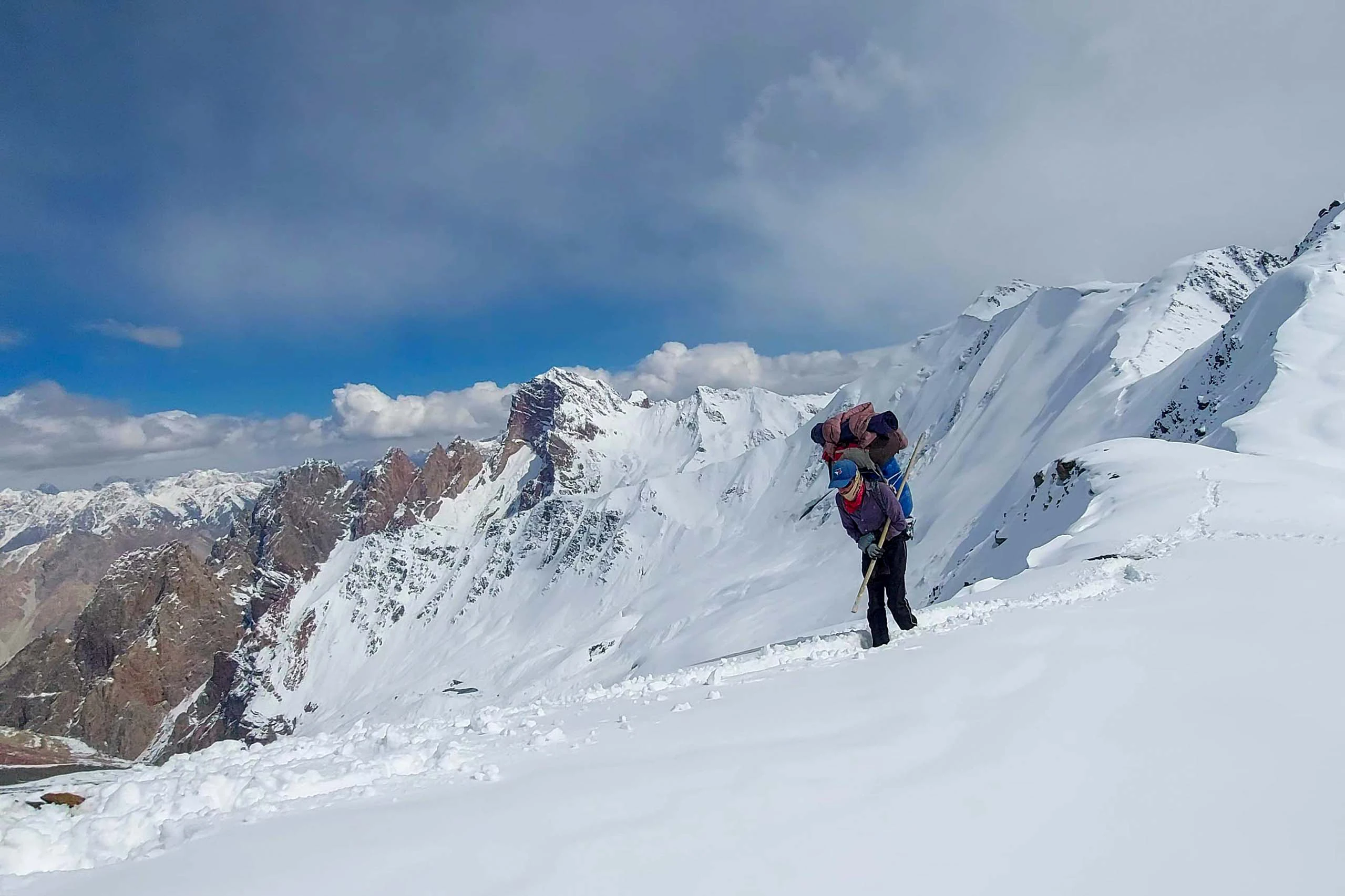 Wandelaar klimt door een besneeuwde helling met hoge bergen op de achtergrond